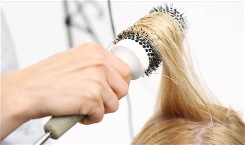 Bạn cần chia tóc thành các lớp và dùng lược tròn để quấn quanh tóc trước khi làm thẳng tóc