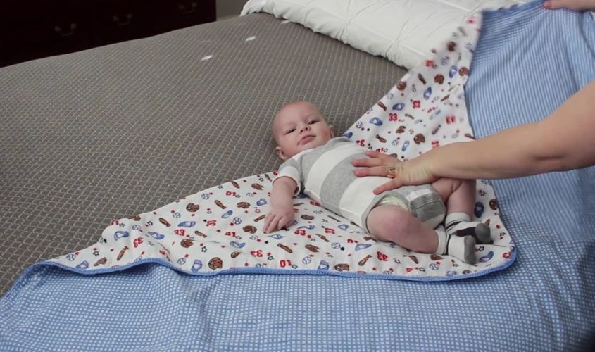 Đặt bé nằm giữa tã sao cho vai nằm bé ngang bằng với mép trên cùng