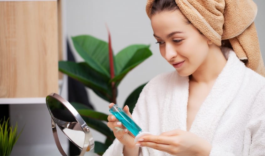 Lấy nước hoa hồng ra bông tẩy trang rồi thoa đều lên mặt