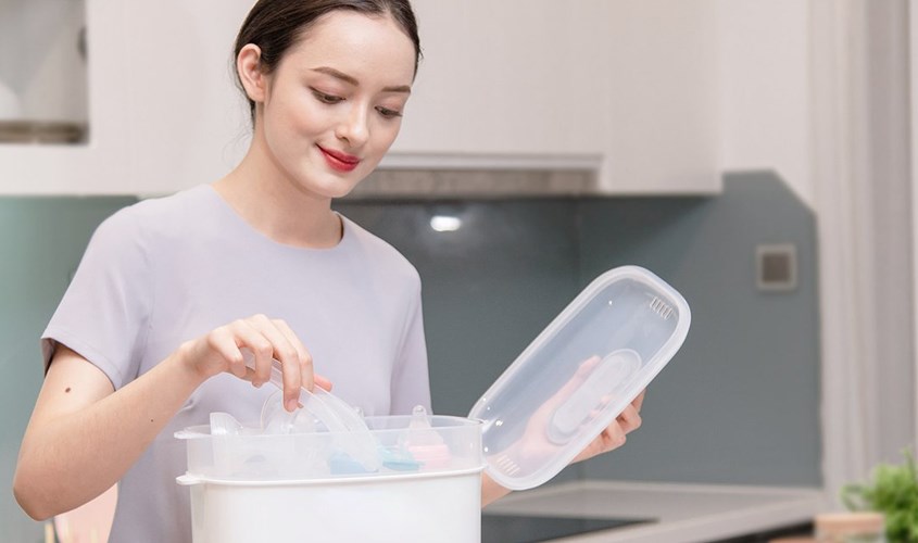 Sử dụng kẹp gắp đi kèm theo máy để lấy bình sữa và đồ dùng ra