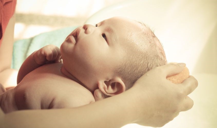Cho bé nằm ngửa ra khi gội đầu để tránh sữa tắm gội rơi vào mắt bé