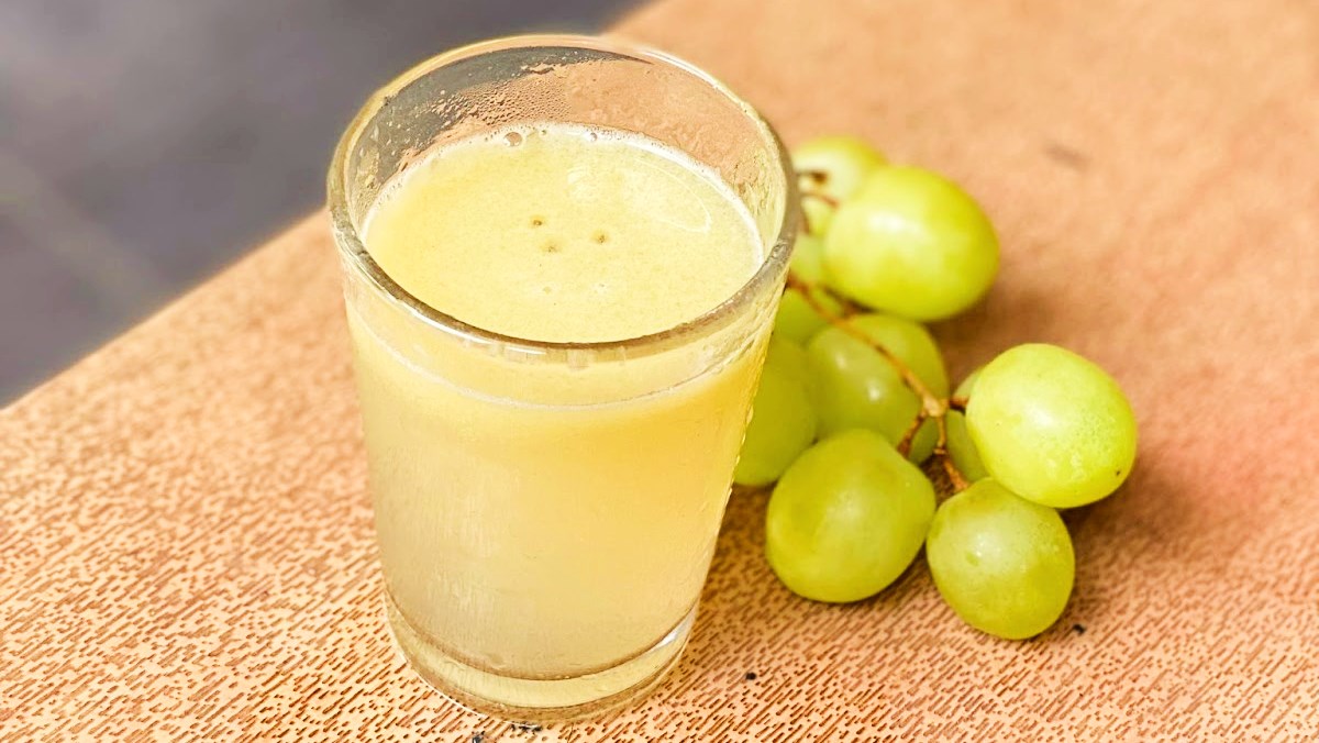 Ly nước ép nho tươi trên bàn, bên cạnh là chùm nho xanh.