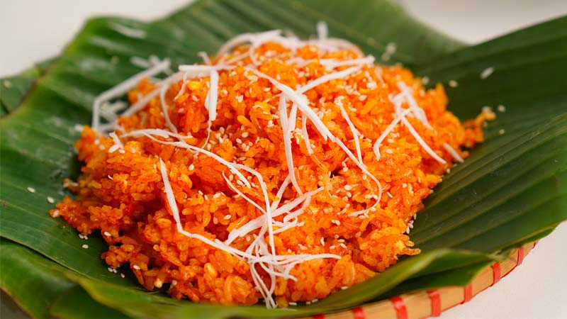 a plate of xoi gac (Vietnamese red sticky rice) served with Vietnamese ham.