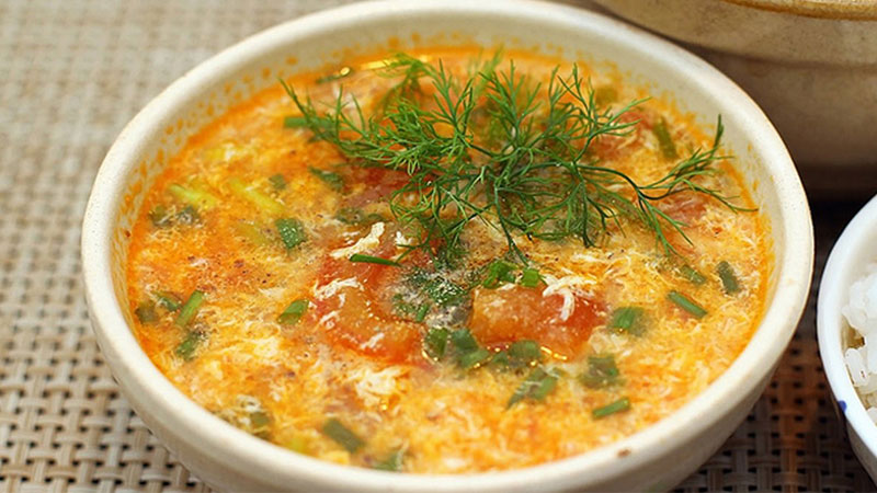 Canh trứng cà chua đã xong rồi, múc ra tô, cho thêm một ít hành ngò lên để trang trí.