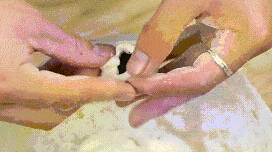 Sau đó chia bột thành những viên đều, ấn dẹp miếng bột và cho nhân mè đen vào rồi gói kín lại.