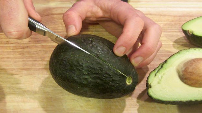 Đặt quả bơ lên thớt theo chiều dọc, dùng dao cắt một đoạn từ phần đỉnh quả bơ xuống dưới đáy