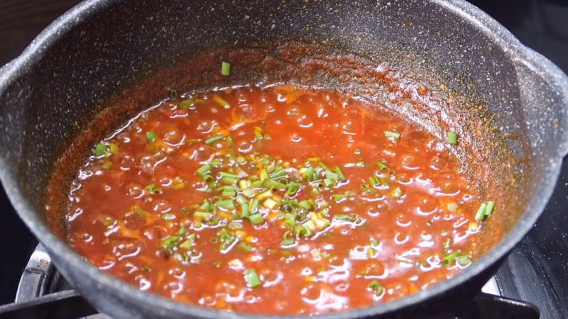 Trộn đều cho các gia vị thấm đều, nấu đến khi cà chua chín mềm thì tắt bếp, cho hành lá lên để sốt có màu đẹp và bắt mắt hơn