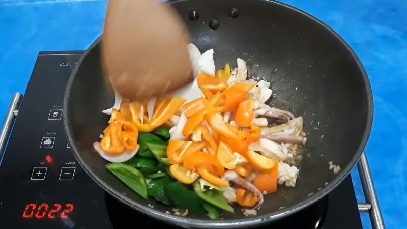 Đảo đều cho gia vị thấm vào mực, rồi cho ớt chuông và hành tây vào, xào ở lửa lớn.