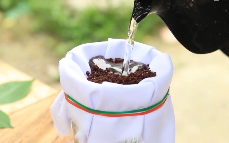 Bước 2: Dùng thun để buộc lại lớp vải này với miệng ly, dùng nước sôi chế vào để tinh chất cà phê chảy ra