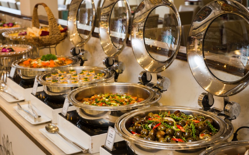 Món chính ăn nóng được để trong nồi buffet, cùng với rau, củ, quả được trưng bày trên các kệ inox