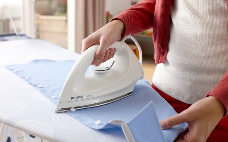 Using an ironing board to iron clothes before drying to make them dry faster