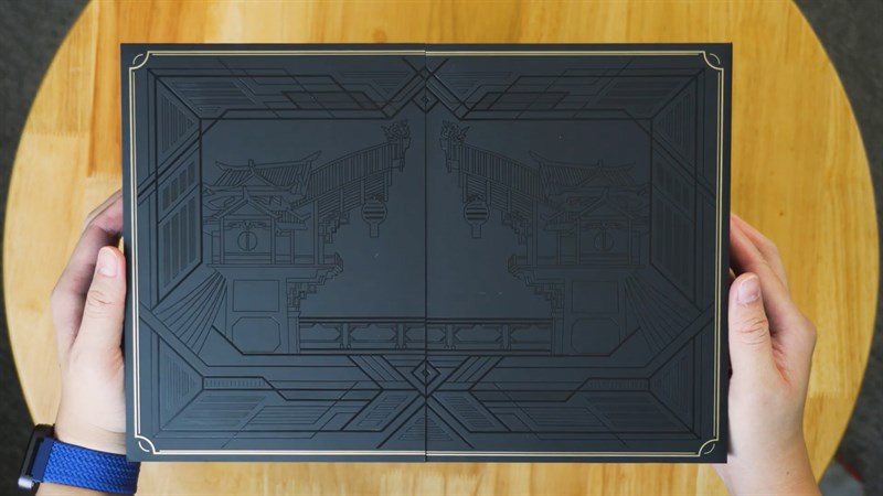 Sau khi mở hộp đỏ thì sẽ đến phần bìa cứng có khắc họa tiết cổng vào phố cảng Liyue Sau khi mở hộp đỏ thì sẽ đến phần bìa cứng có khắc họa tiết cổng vào phố cảng Liyue